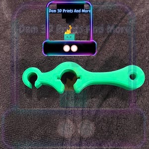 以下が含まれることがあります： 鮮やかな緑色の3Dプリントツール。湾曲した端、中央の開口部、反対側の穴が特徴です。このツールは、特定の機能、おそらくオブジェクトを開いたり操作したりするために設計されています。「Dem 3D Prints And More」のテキストも表示されています。