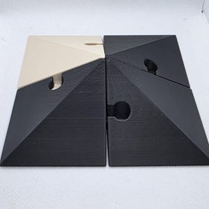 Pode incluir: Quebra-cabe&ccedil;a de quatro pe&ccedil;as com um design geom&eacute;trico. O quebra-cabe&ccedil;a &eacute; composto por quatro pe&ccedil;as triangulares interligadas. Duas pe&ccedil;as s&atilde;o pretas e duas s&atilde;o branco-sujo. Cada pe&ccedil;a tem um entalhe curvo para interliga&ccedil;&atilde;o.