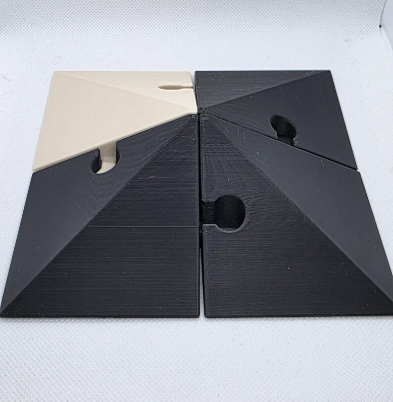 Pode incluir: Quebra-cabe&ccedil;a de quatro pe&ccedil;as com um design geom&eacute;trico. O quebra-cabe&ccedil;a &eacute; composto por quatro pe&ccedil;as triangulares interligadas. Duas pe&ccedil;as s&atilde;o pretas e duas s&atilde;o branco-sujo. Cada pe&ccedil;a tem um entalhe curvo para interliga&ccedil;&atilde;o.