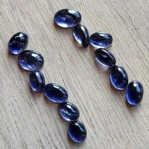 Peut inclure: Une collection de onze pierres précieuses cabochons bleu profond, lisses et de forme ovale, disposées en deux lignes séparées légèrement incurvées. Chaque pierre présente une surface polie et réfléchissante aux nuances indigo et bleu violet.