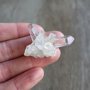 May include: A cluster of clear quartz crystals with a pointed shape. The crystals are arranged in a cluster, with some of the points facing upwards and others facing downwards.