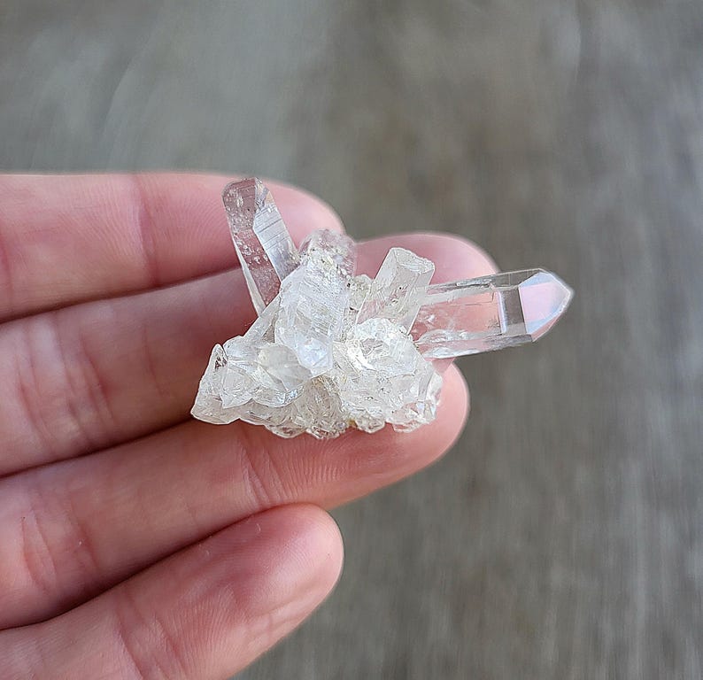 May include: A cluster of clear quartz crystals with a pointed shape. The crystals are arranged in a cluster, with some of the points facing upwards and others facing downwards.