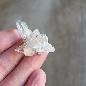 May include: A cluster of clear quartz crystals with a pointed shape. The crystals are arranged in a cluster, with some of the crystals pointing upwards and others pointing downwards.
