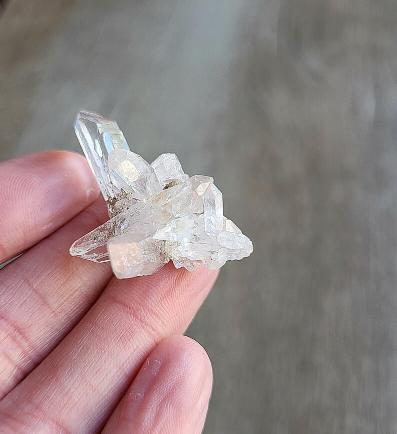 May include: A cluster of clear quartz crystals with a pointed shape. The crystals are arranged in a cluster, with some of the crystals pointing upwards and others pointing downwards.