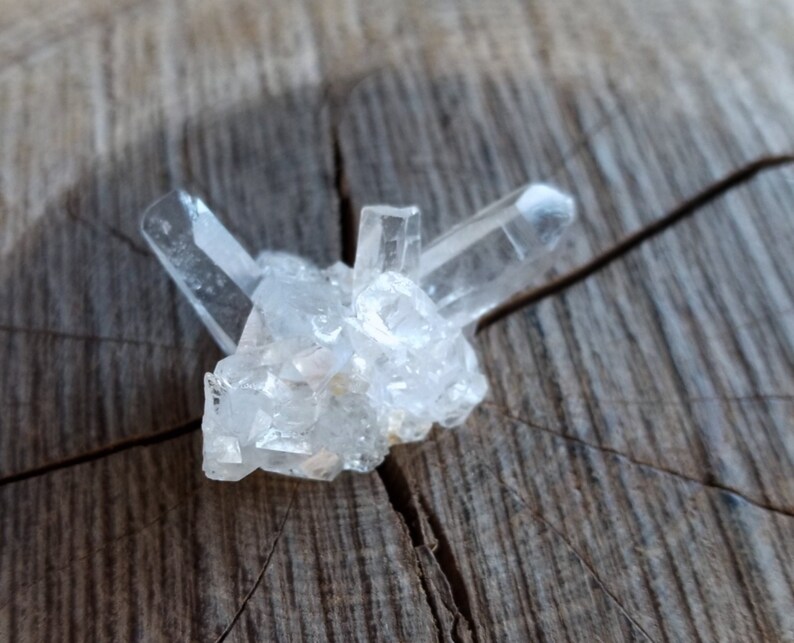 May include: A cluster of clear quartz crystals on a rough wooden surface.