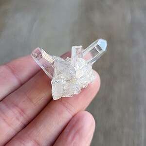 May include: A cluster of clear quartz crystals with a pointed shape. The crystals are arranged in a cluster, with some of the points facing upwards.