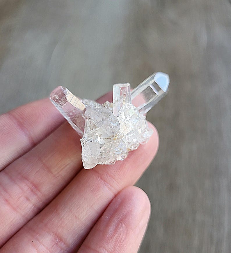 May include: A cluster of clear quartz crystals with a pointed shape. The crystals are arranged in a cluster, with some of the points facing upwards.