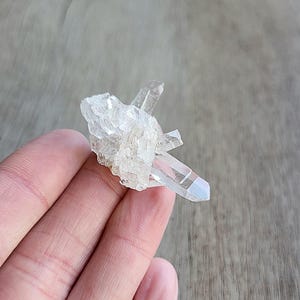 May include: A small cluster of clear quartz crystals with a rainbow iridescent effect. The crystals are clustered together in a natural formation.