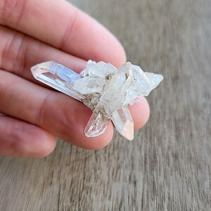 May include: A cluster of clear quartz crystals with a pointed shape. The crystals are arranged in a cluster, with some of the points facing upwards and others facing downwards.