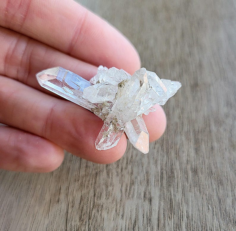 May include: A cluster of clear quartz crystals with a pointed shape. The crystals are arranged in a cluster, with some of the points facing upwards and others facing downwards.