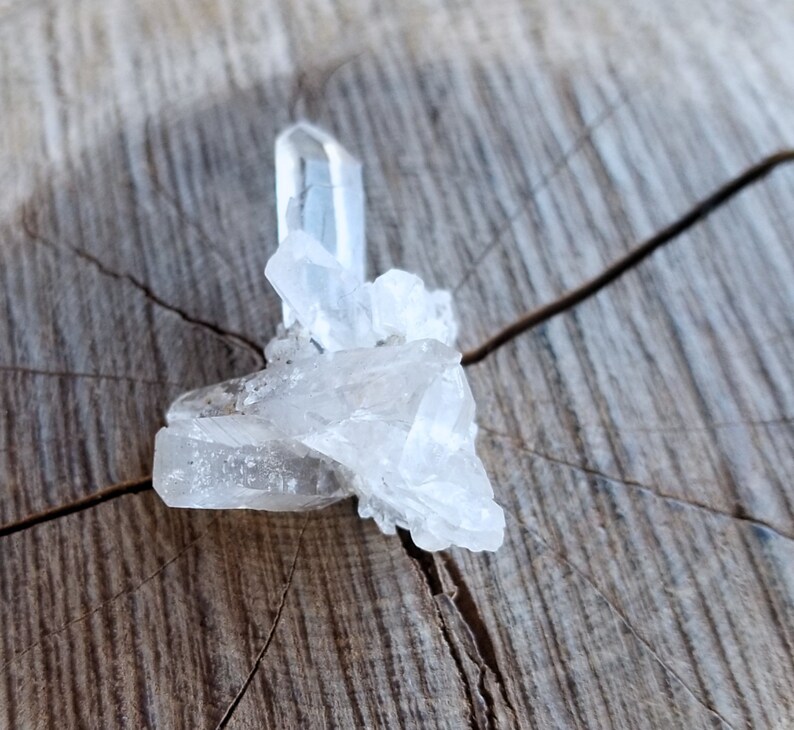 May include: A cluster of clear quartz crystals on a rough wooden surface. The crystals are arranged in a loose, organic shape, with some of the points facing upwards.
