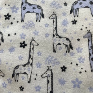 May include: A white fabric with a repeating pattern of black giraffes and purple flowers. The giraffes have black spots and the flowers have a light purple outline.