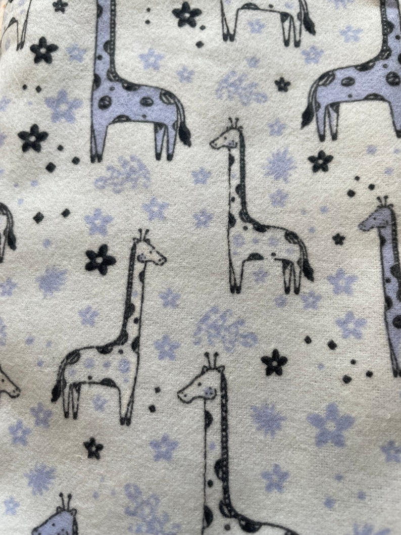 May include: A white fabric with a repeating pattern of black giraffes and purple flowers. The giraffes have black spots and the flowers have a light purple outline.