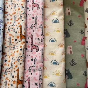 May include: A collection of six fabric swatches featuring different animal and nature-themed patterns. The swatches include a light blue fabric with giraffes, a beige fabric with giraffes, a pink fabric with giraffes, a beige fabric with suns, a green fabric with bears and trees, and a beige fabric with bears and mushrooms.