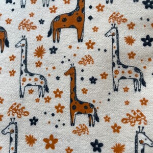 May include: A white fabric with a repeating pattern of brown and black giraffes, brown flowers, and black and brown leaves.