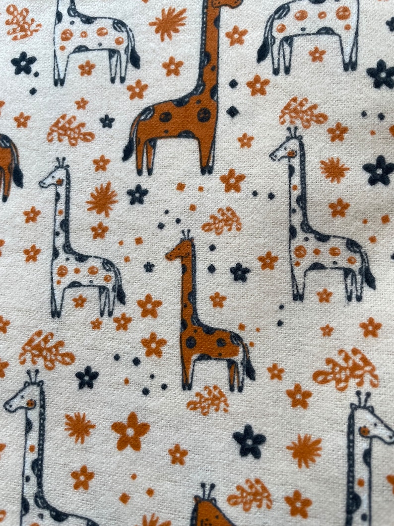 May include: A white fabric with a repeating pattern of brown and black giraffes, brown flowers, and black and brown leaves.