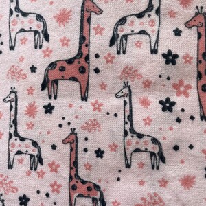 May include: Pink fabric with a repeating pattern of giraffes and flowers. The giraffes are pink and black with white spots. The flowers are pink and black.