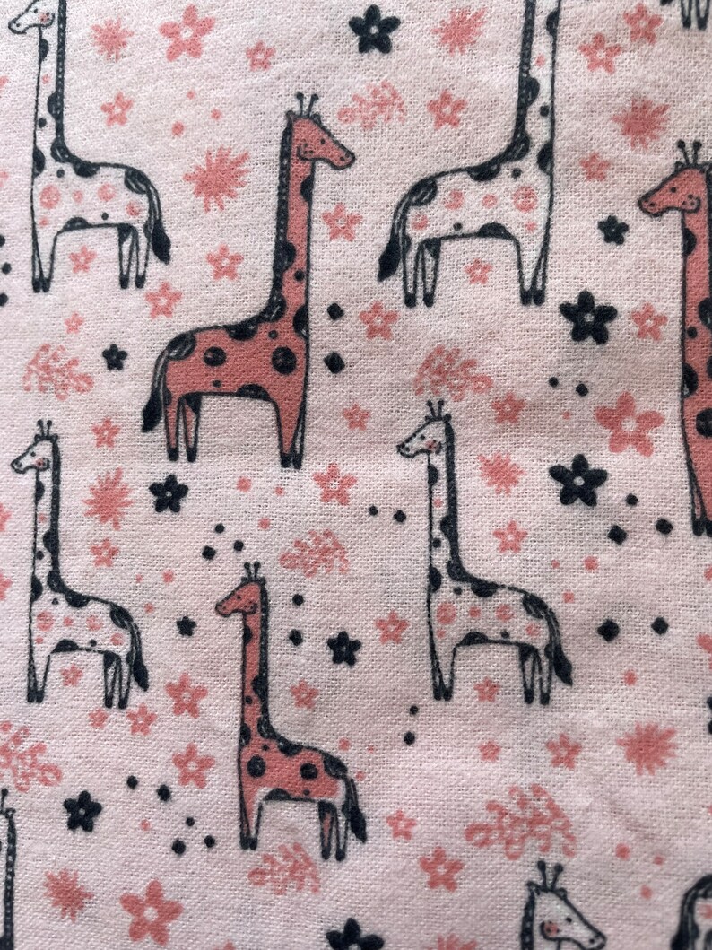 May include: Pink fabric with a repeating pattern of giraffes and flowers. The giraffes are pink and black with white spots. The flowers are pink and black.