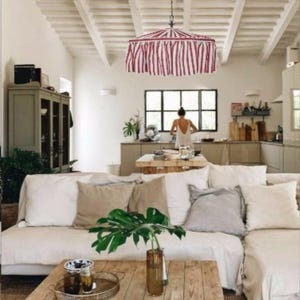 May include: A living room featuring a large white sofa with beige and gray throw pillows, a wooden coffee table with a glass vase containing a green plant, and a red and white striped fabric pendant light hanging from the ceiling.