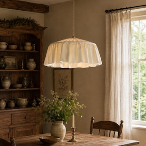 May include: A cream-coloured fabric pendant light fixture featuring a wide, pleated, ruffled shade suspended from a thin, twisted metal cord attached to a matching circular ceiling canopy, providing a soft, diffused downward light.