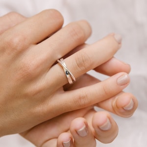 Puede incluir: Primer plano de una mano con un anillo de plata con una pequeña piedra negra. El anillo es una banda simple con un diseño de torsión.
