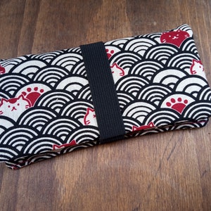 Pode incluir: Uma carteira de tecido preto e branco com um design de gato vermelho e impressão de pata. A carteira tem uma alça preta.