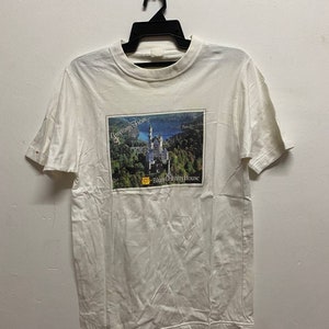 May include: White t-shirt with a printed image of a castle and the text "Greetings From... Blue Country House".