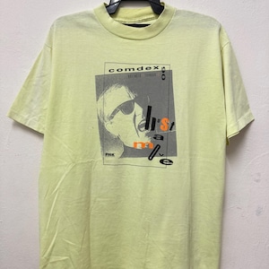 May include: A yellow t-shirt with a black and white graphic print of a person wearing sunglasses and a black and white graphic print of the text "comdex 90" and "h's't m a v e".