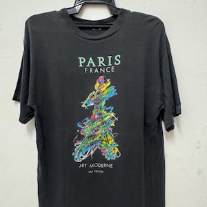 Könnte beinhalten: Schwarzes T-Shirt mit der Aufschrift "PARIS FRANCE" und einem farbenfrohen abstrakten Design, das den Eiffelturm darstellt. Darunter steht "ART MODERNE" und "SAP POLYNE".