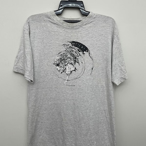 May include: A gray t-shirt with a black and white graphic print of a creature with wings. The graphic is in a circle with the text "Devilish" at the bottom.