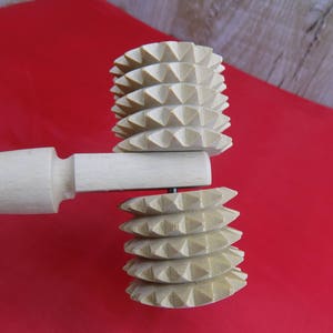 May include: A wooden rolling pin with two interchangeable heads. The heads are made of wood and have a textured, spiked design. The rolling pin is a kitchen tool used for rolling out dough.