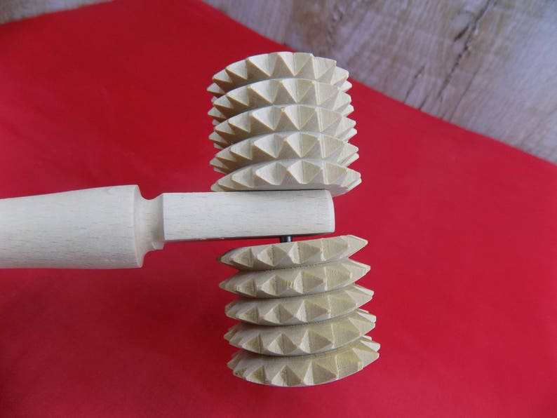May include: A wooden rolling pin with two interchangeable heads. The heads are made of wood and have a textured, spiked design. The rolling pin is a kitchen tool used for rolling out dough.