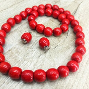 May include: A red wooden bead necklace, bracelet, and earrings set. The beads are large and round, and the jewelry is made of natural wood.