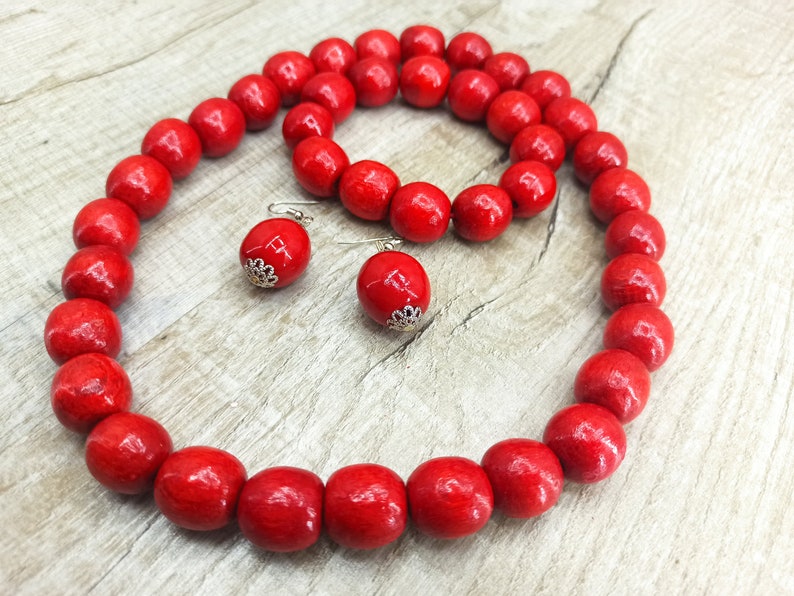 May include: A red wooden bead necklace, bracelet, and earrings set. The beads are large and round, and the jewelry is made of natural wood.