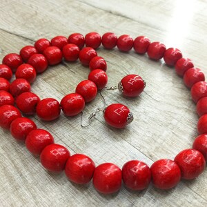 May include: A red wooden bead necklace and bracelet set with matching earrings. The beads are large and round, and the earrings have silver hooks.