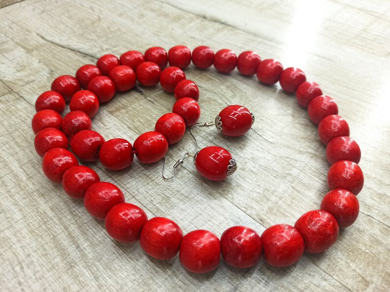 May include: A red wooden bead necklace and bracelet set with matching earrings. The beads are large and round, and the earrings have silver hooks.
