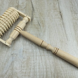May include: A wooden massage roller with a handle and a wheel of spikes. The roller is made of light brown wood and the spikes are made of a darker wood.