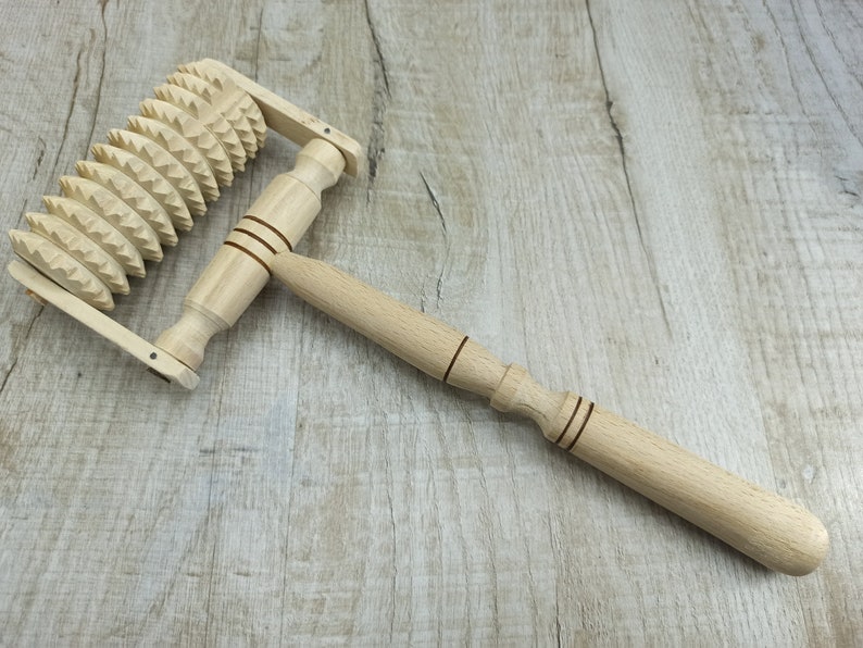 May include: A wooden massage roller with a handle and a wheel of spikes. The roller is made of light brown wood and the spikes are made of a darker wood.