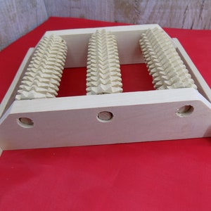 May include: A wooden foot roller with three rollers, each with a textured surface. The roller is designed to help with foot massage and relaxation.