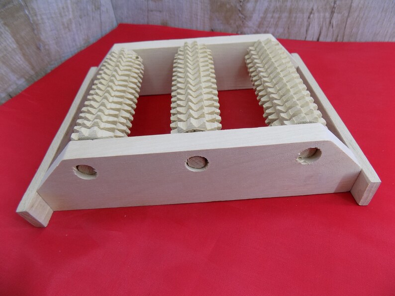 May include: A wooden foot roller with three rollers, each with a textured surface. The roller is designed to help with foot massage and relaxation.