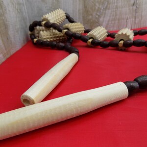May include: A wooden massage tool with multiple rollers connected by brown beads. The tool has two wooden handles.