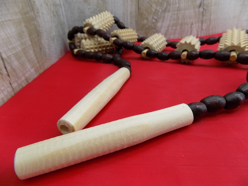 May include: A wooden massage tool with multiple rollers connected by brown beads. The tool has two wooden handles.