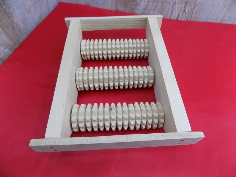 May include: A wooden foot roller with three rows of spiked rollers. The roller is made of natural wood and has a light brown colour.