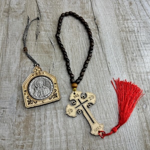 May include: A wooden cross with the text "NIKA" and "IC XC" on it, a wooden icon with a silver image of a person, and a brown wooden rosary with a tassel.
