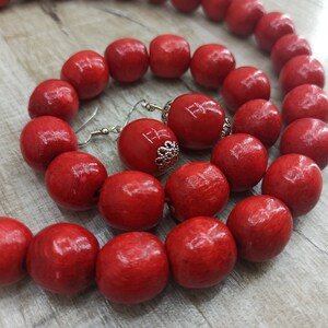May include: A red wooden bead necklace and earrings set. The necklace is made of large, round beads and the earrings are simple and dangle.