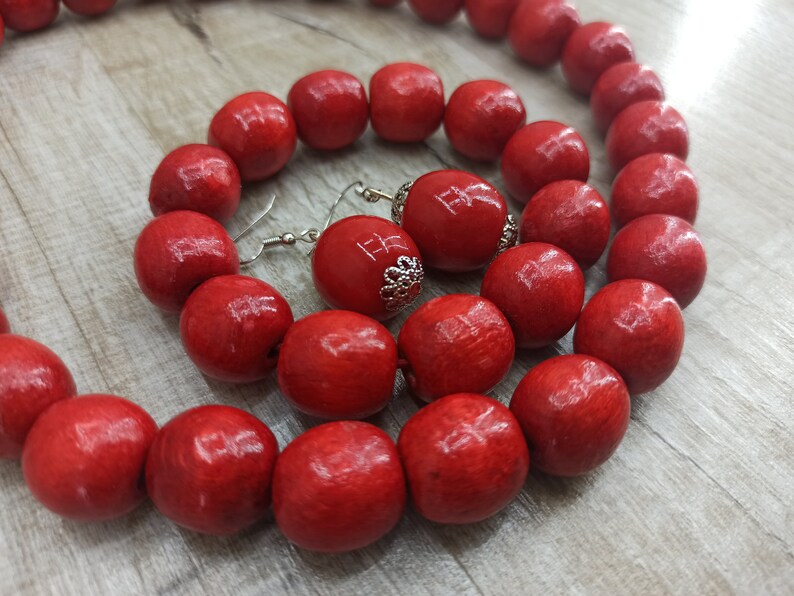 May include: A red wooden bead necklace and earrings set. The necklace is made of large, round beads and the earrings are simple and dangle.