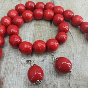 May include: A red wooden bead necklace and earrings set. The necklace is made of large, round beads and the earrings are simple and dangle.