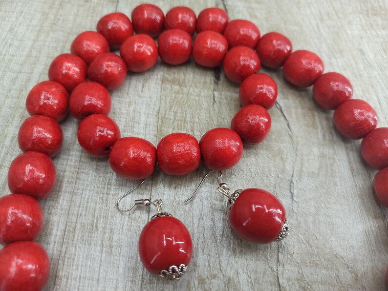 May include: A red wooden bead necklace and earrings set. The necklace is made of large, round beads and the earrings are simple and dangle.
