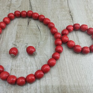 May include: A red wooden bead necklace, bracelet, and earrings set. The necklace and bracelet are made of large, round beads. The earrings are simple silver hoops with a red bead at the end.
