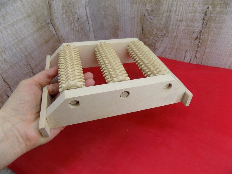 May include: Wooden foot massage roller with three rollers. The rollers have a textured surface and are mounted on a wooden frame.